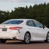 A whit 2018 Toyota Camry is parked in front of pine trees in right rear corner view