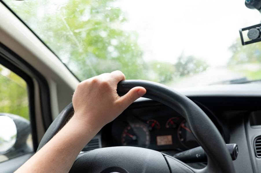 A driver with incorrect hand placement committing one of the most common driving mistakes.