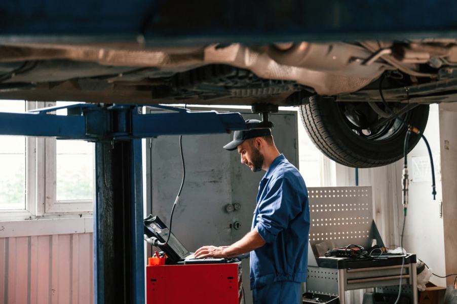 Mechanics working at a shop using a plug-in module for a car on a lift.