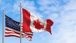 An American and a Canadian flag fly above a car park.