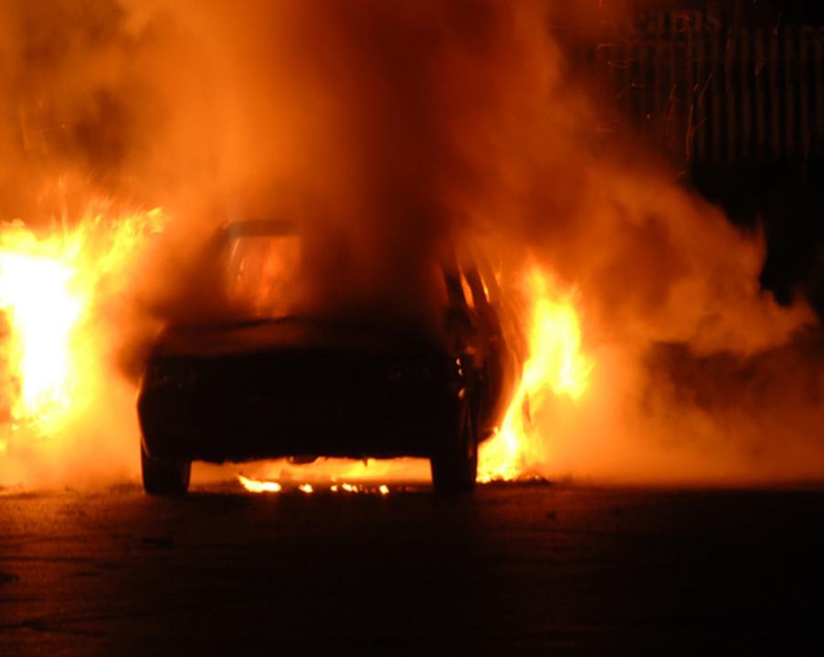 A firefighter approaches a raging car fire.