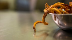 Curly fries in a bowl, spilling onto a table