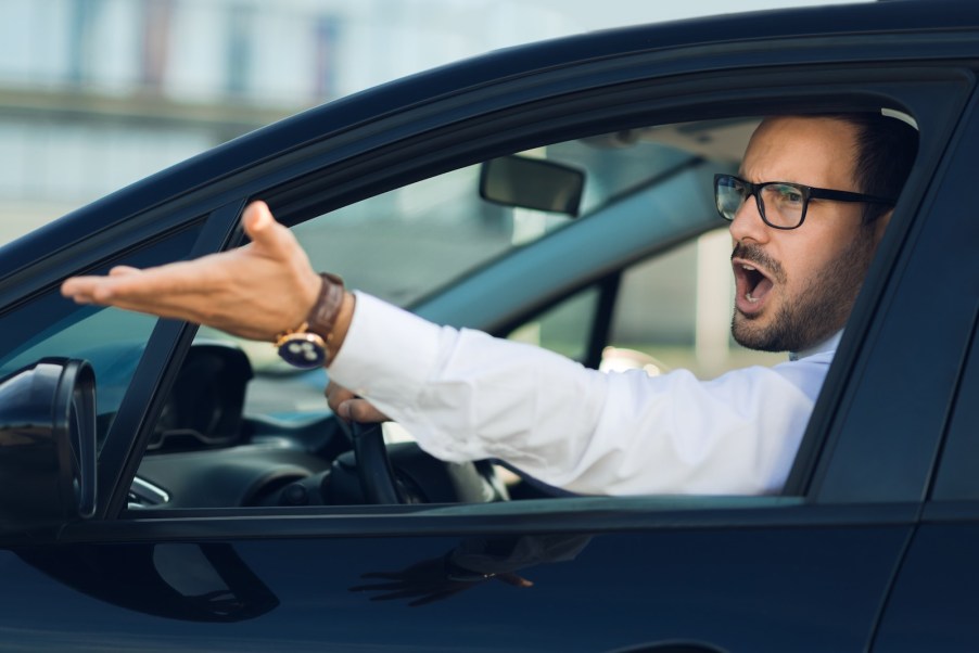 Man with glasses and white shirt gesturing while driving in road rage traffic.