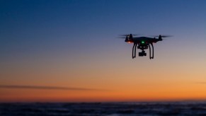 A drone takes off at sunset, cruising above a landscape.