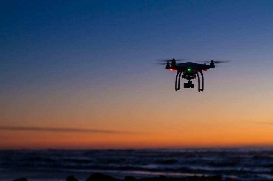 A drone takes off at sunset, cruising above a landscape.