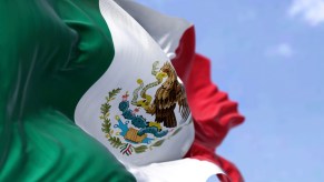 The national flag of Mexico, waving in front of a blue sky.