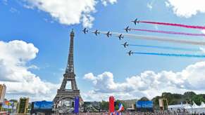 Squadron of French fighter jets fly by the Eiffel Tower in Paris while crowds watch on.