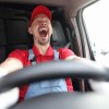 Man driving a car with a big smile on his face, hands on steering wheel in the foreground.