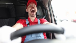 Man driving a car with a big smile on his face, hands on steering wheel in the foreground.