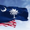 The South Carolina state flag and U.S. National flag in front of a blue sky.