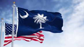 The South Carolina state flag and U.S. National flag in front of a blue sky.