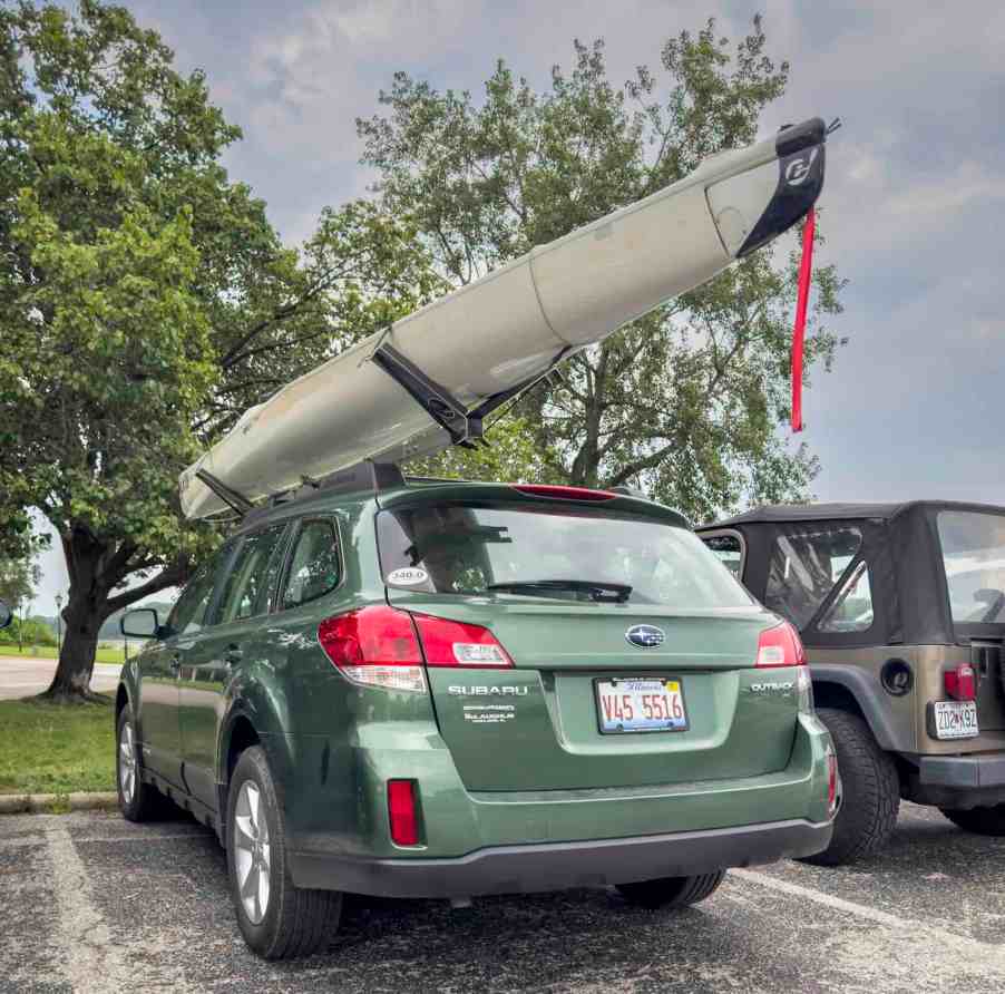 Back of a green Subaru Outback AWD crossover in a parking lot with a kayak on the roof.