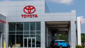 Vintage Toyota SUV below a dealership sign full of hybrids trucks and crossover.