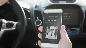 Hand holding a cell phone inside a car playing a music track connected to Bluetooth in close view