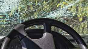 A crashed car parked in a green wooded area in close driver interior view of the steering wheel and cracked windshield