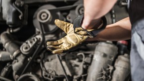 Diesel mechanic putting on leather work gloves in front of open engine view from elbows to knees