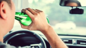 Driver drinking beer from a green bottle.