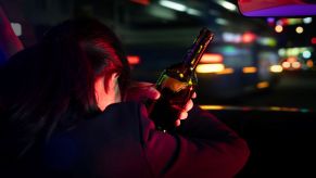 A woman driving drunk, holding a bottle of alcohol in her hands