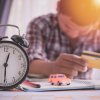 Man depicting late car loan payment holding head and credit card on desk with clock, toy car, and papers