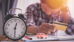 Man depicting late car loan payment holding head and credit card on desk with clock, toy car, and papers