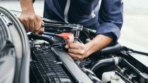 Mechanic shown from shoulders down working on a car engine in close view