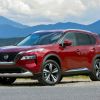 A red Nissan Rogue SUV parked in right front angle view with mountains in the background