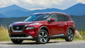 A red Nissan Rogue SUV parked in right front angle view with mountains in the background