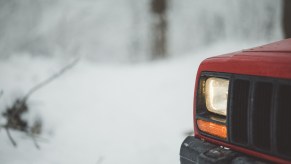 The right front corner of a red Jeep parked in snowy outdoors