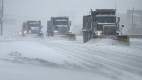 Three snow plow trucks driving on snow-covered freeway