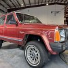 A rust-colored 1985 Jeep XJ Cherokee parked in low right front angle view in a garage