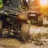 Two ATV riders crossing a dirt road, the setting sun in the background.