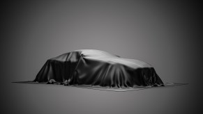 Dependable luxury car under a black cover cloth in front of a gray background.