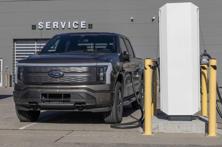 Ford F-150 Lightning electric truck at an EV charger, a "service" sign in the background.