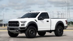 White, regular cab Ford F-150 with a Raptor-like lift kit parked in a lot, power lines in the background.