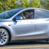 Jay Leno test driving a new Tesla Model Y, trees visible in the background.