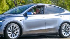 Jay Leno test driving a new Tesla Model Y, trees visible in the background.