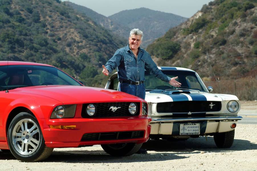 Collector Jay Leno stands between a pre-smog and post-smog Ford Mustang, mountains in the background