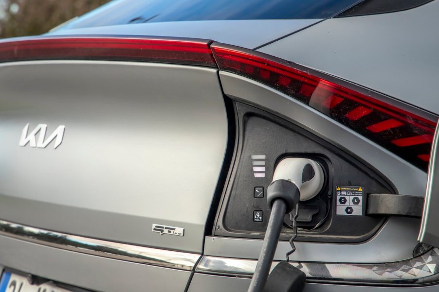 Closeup of the Kia badge on an EV6 plugged into a Tesla supercharger.