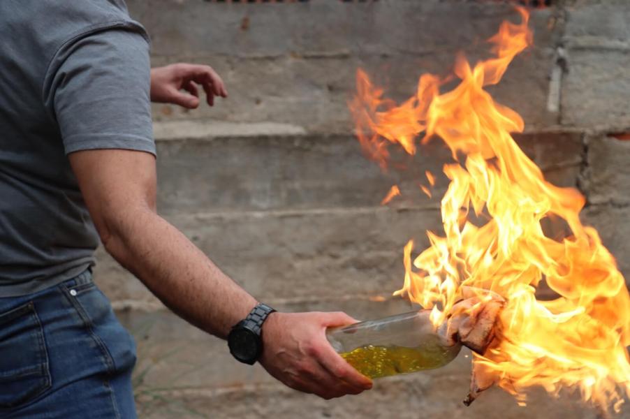 An arsonist prepares to light Tesla EVs on fire with a Molotov cocktail.