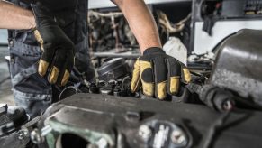 The hands of a Toyota Tundra mechanic trying to fix a seized motor.