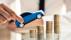 Hands holding an SUV pointed up over stacks of coins to show the soaring used prices of several models.