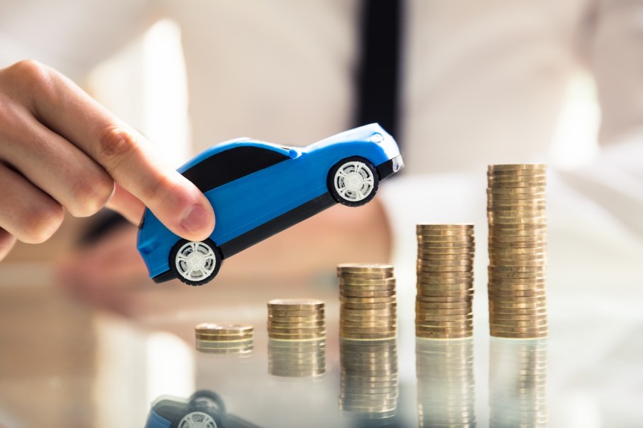 Hands holding an SUV pointed up over stacks of coins to show the soaring used prices of several models.