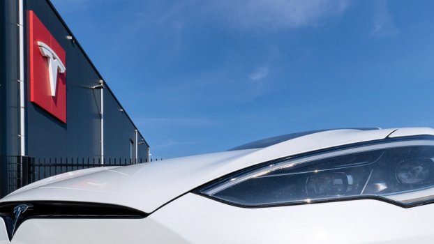 A Tesla Model S near a storefront with its badge prominently displayed.