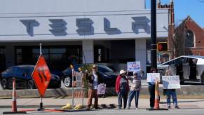 Protesters gather outside of a Tesla dealership.