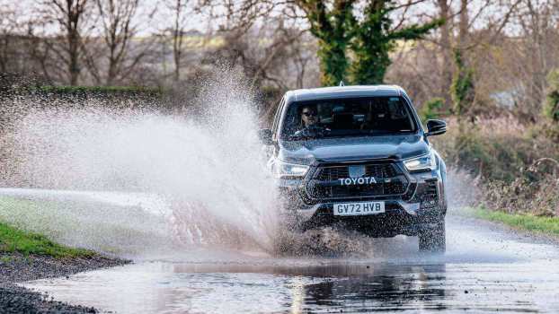 A Toyota Hilux GR pickup truck kicking up water on a trail.