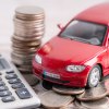 Red toy car on a pile of coins next to a calculator a buyer is using to figure out used car loan interest rates.