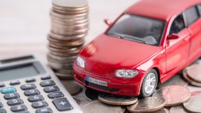 Red toy car on a pile of coins next to a calculator a buyer is using to figure out used car loan interest rates.