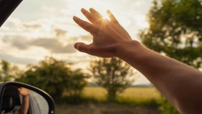 An arm reaching out of open car window in close view at dusk