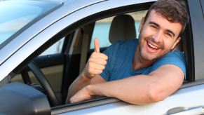 A driver in a car wearing blue short gives thumbs up signal