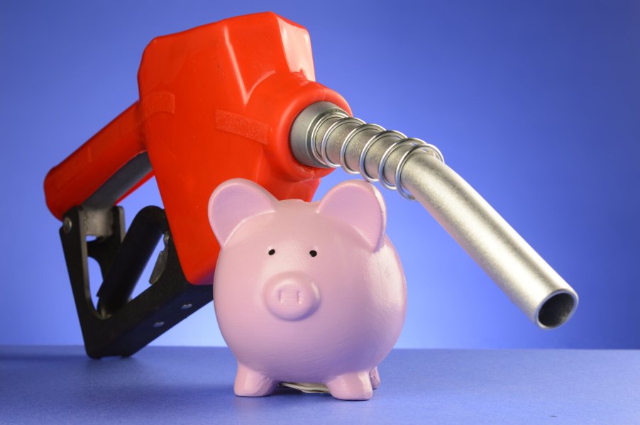 A red gas pump nozzle rests on top of a pink piggy bank with blue background